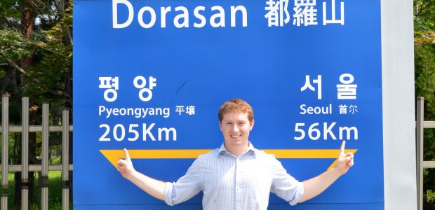 Jesse Clark in front of a sign noting the distance between Pyeongyang and Seoul at the DMZ
