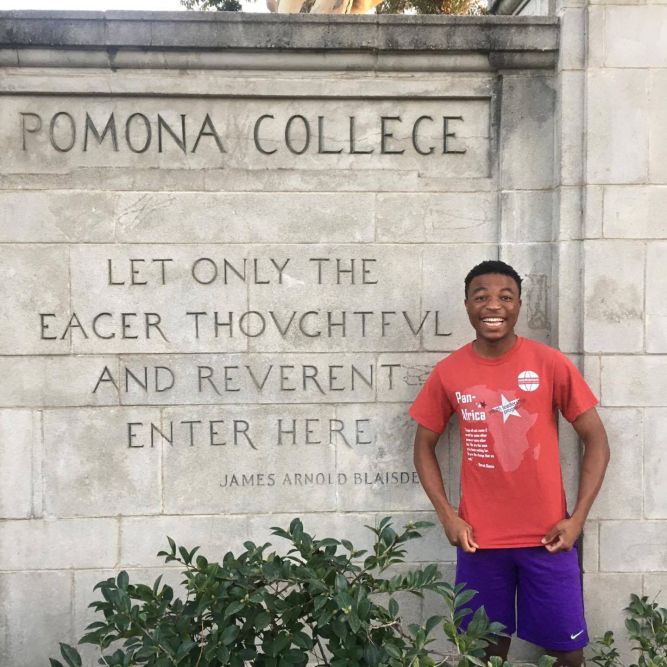 Brian Sibanda poses in a PAYLP t-shirt in front of Pomona College